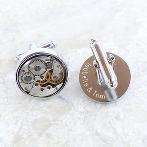 May include: A pair of silver cufflinks. One cufflink features a visible watch mechanism, while the other is engraved with the text "Isobelle & Tom".