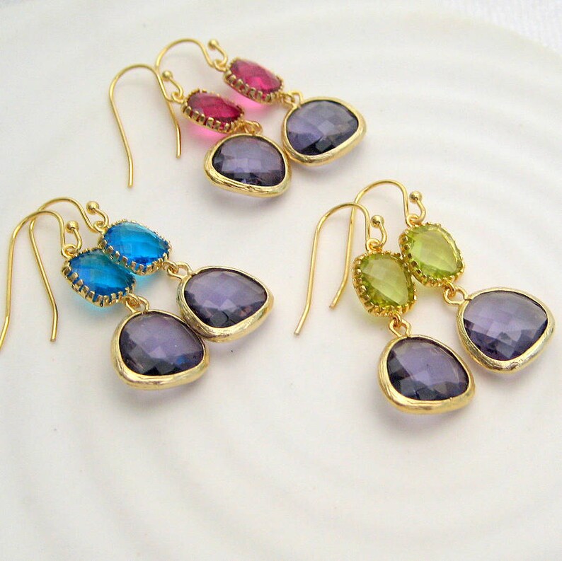 Pu&ograve; includere: Tre paia di orecchini pendenti con ganci dorati e due cristalli a forma di goccia. Gli orecchini presentano una variet&agrave; di colori, tra cui viola, verde, blu e rosa.