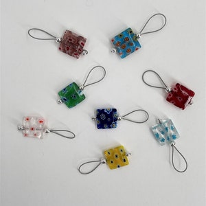 May include: Nine colorful glass squares with different patterns, each attached to a silver loop and a silver cord. The squares are in shades of blue, green, red, yellow, and white.