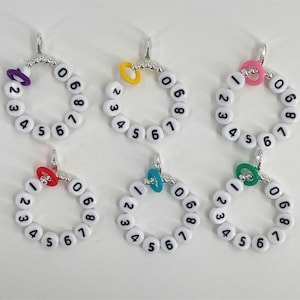 May include: Set of ten white plastic rings with numbers 0-9 printed on them. Each ring has a small silver loop at the top and a colored plastic ring in the center. The colors are purple, yellow, pink, red, and turquoise.
