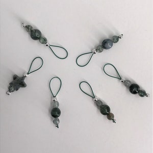 Puede incluir: Seis marcadores de punto verde y plata con diferentes cuentas de piedras preciosas. Los marcadores est&aacute;n hechos de el&aacute;stico verde y anillos met&aacute;licos plateados.