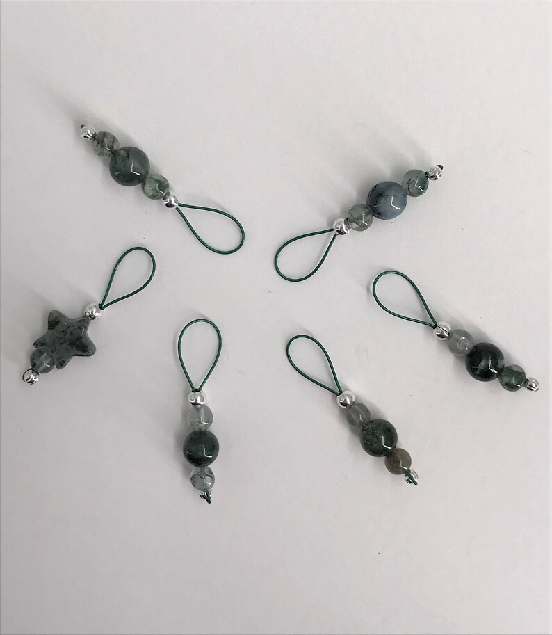 Puede incluir: Seis marcadores de punto verde y plata con diferentes cuentas de piedras preciosas. Los marcadores est&aacute;n hechos de el&aacute;stico verde y anillos met&aacute;licos plateados.