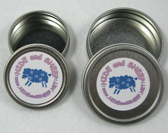 Puede incluir: Dos latas de metal plateadas con tapas. Las latas tienen una etiqueta blanca con una oveja azul y el texto "HIDE and SHEEP | www.HIDEandSHEEP.NET".