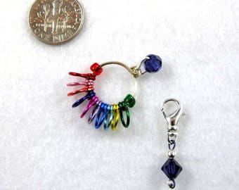 Puede incluir: Un anillo de marcador de punto de color arcoíris con un amuleto de cristal morado y un broche de langosta plateado con un amuleto de cristal morado.