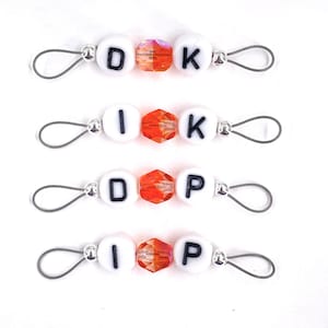 May include: Four sets of white letter beads with orange crystal beads and silver metal loops. The beads spell out "DOK", "IK", "DOP", and "IP".
