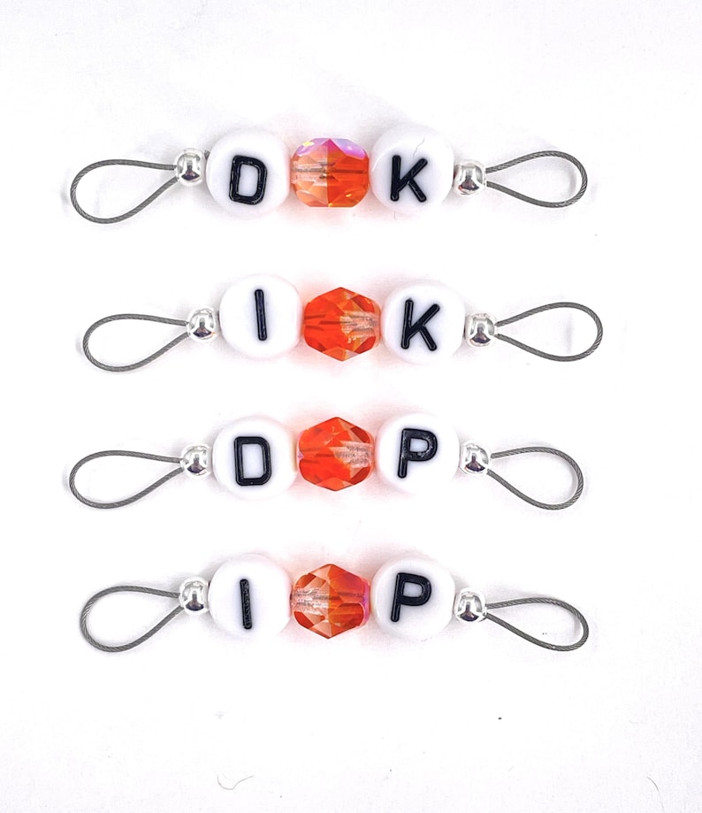 May include: Four sets of white letter beads with orange crystal beads and silver metal loops. The beads spell out "DOK", "IK", "DOP", and "IP".