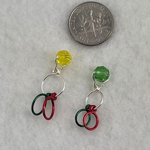 May include: Two silver wire stitch markers with red and green loops and a yellow and green glass bead at the top.