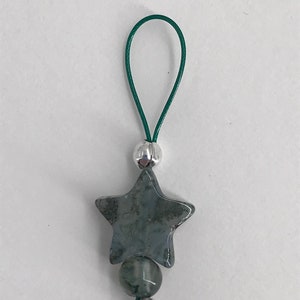 Puede incluir: Un amuleto de estrella verde y plateado con un cord&oacute;n verde. La estrella est&aacute; hecha de una piedra verde con detalles plateados.