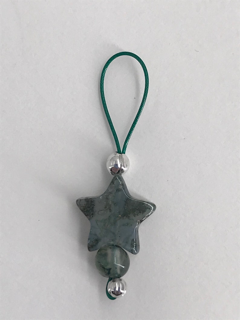 Puede incluir: Un amuleto de estrella verde y plateado con un cord&oacute;n verde. La estrella est&aacute; hecha de una piedra verde con detalles plateados.