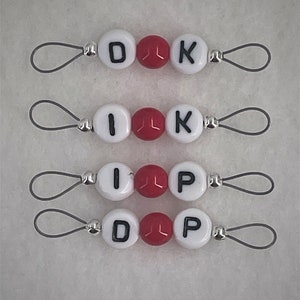 May include: Four sets of white and red bead charms with letter beads spelling out "DIK", "IK", "IP", and "DP". Each charm has a silver loop.