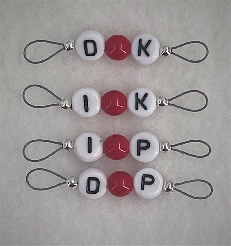 Puede incluir: Cuatro juegos de abalorios de cuentas blancas y rojas con cuentas de letras que deletrean "DIK", "IK", "IP" y "DP". Cada abalorio tiene un lazo plateado.