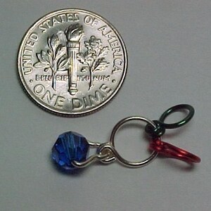 Pu&ograve; includere: Una moneta da dieci centesimi americana in argento con le parole "United States of America" e "One Dime" su di essa. Una perla di vetro blu &egrave; attaccata a un anello d'argento con filo rosso e verde.