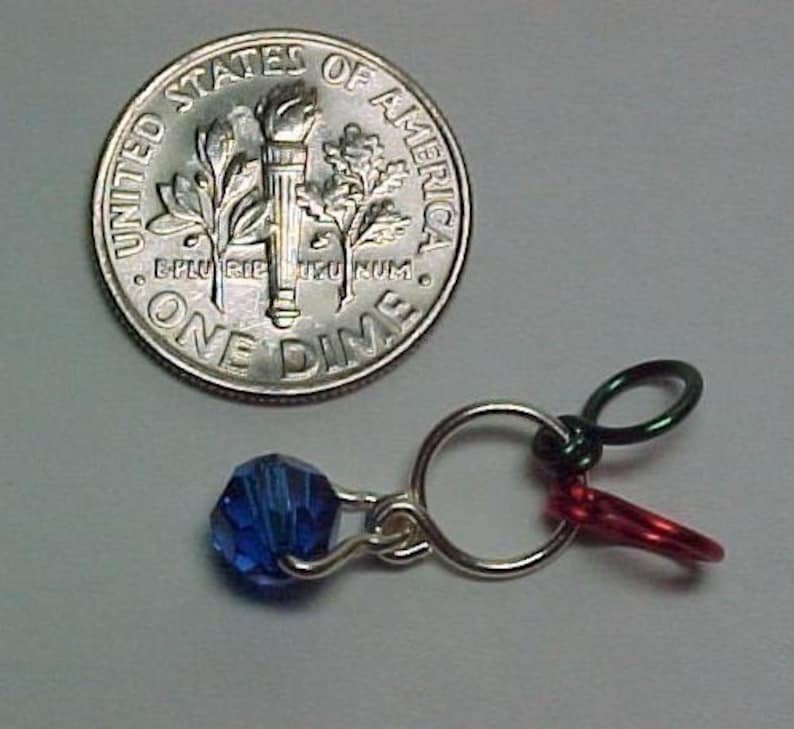 Pu&ograve; includere: Una moneta da dieci centesimi americana in argento con le parole "United States of America" e "One Dime" su di essa. Una perla di vetro blu &egrave; attaccata a un anello d'argento con filo rosso e verde.