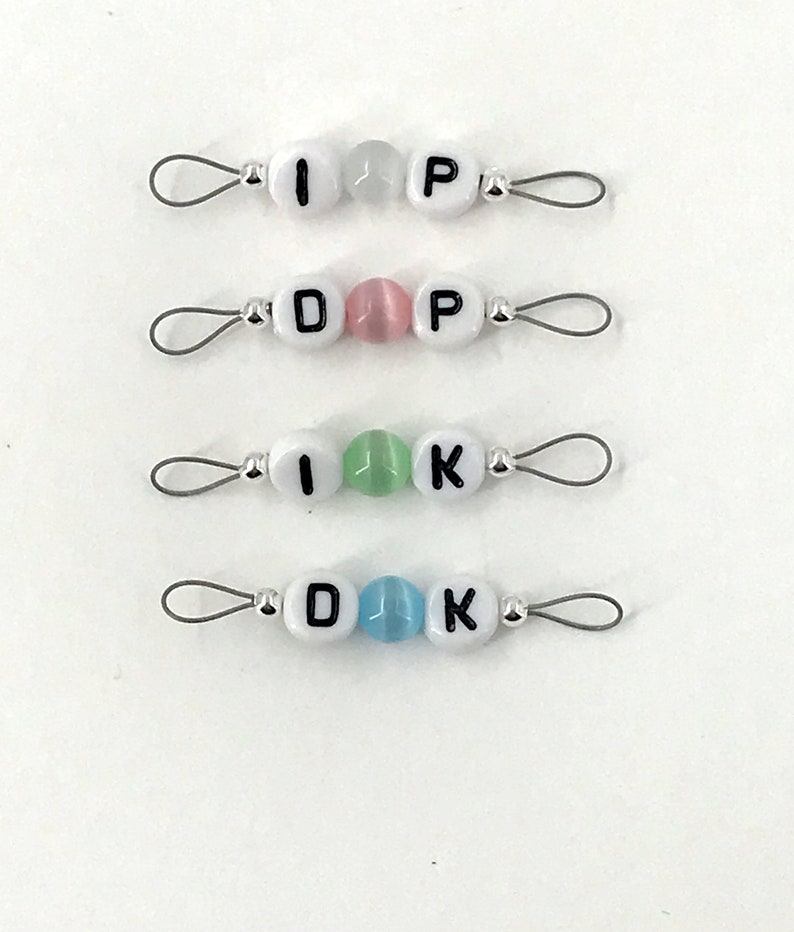 May include: Four sets of white letter beads on silver wire with loops at each end. The beads spell out "I P", "D P", "I K", and "D K". The beads are separated by colored beads: white, pink, green, and blue.