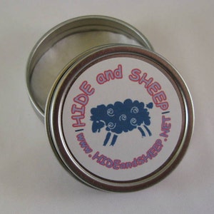 May include: A silver tin with a white lid and a blue and white sheep illustration on the label. The label reads "Hide and Sheep | www.HideandSheep.net".