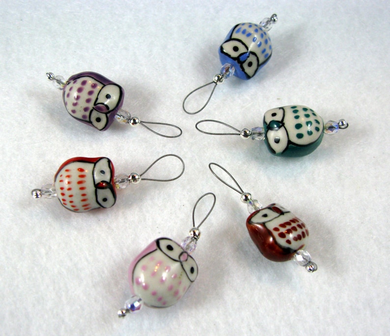 May include: Six owl-shaped thread spool holders with clear crystal beads. Each owl is a different color and pattern: purple, orange, blue, green, pink, and brown.