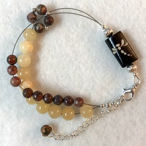 May include: A double-strand bracelet with brown and yellow beads and a black dragonfly charm. The bracelet has a silver clasp.