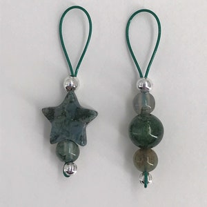 Puede incluir: Dos colgantes de amuleto de &aacute;gata verde con cuentas plateadas y lazos de cuerda verde. Un colgante presenta una piedra en forma de estrella y el otro tiene tres piedras redondas.