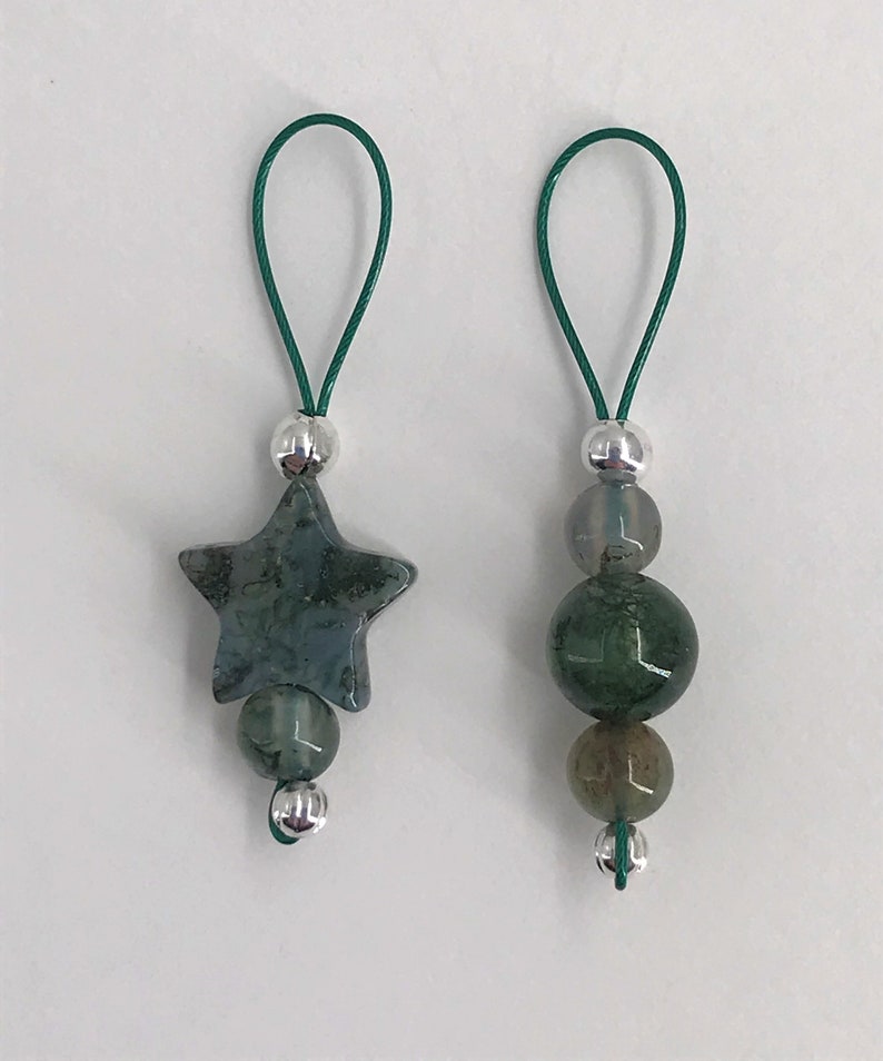 Puede incluir: Dos colgantes de amuleto de &aacute;gata verde con cuentas plateadas y lazos de cuerda verde. Un colgante presenta una piedra en forma de estrella y el otro tiene tres piedras redondas.