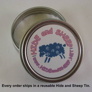 May include: A silver tin with a white label and pink lettering that reads "HIDE and SHEEP" with a blue sheep illustration. The tin is open and the inside is lined with white paper.