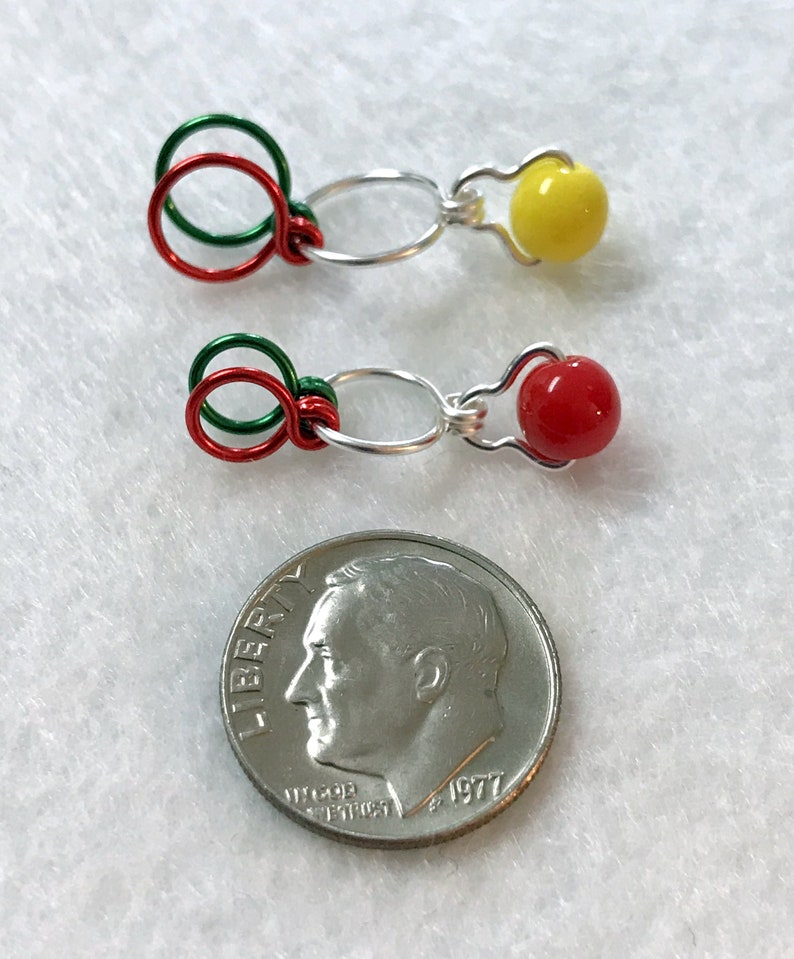 May include: Two silver wire jewelry findings with red, green, and yellow beads. The findings are about the size of a US dime.