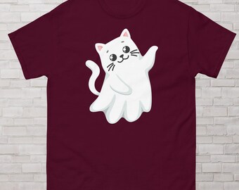 May include: A maroon t-shirt featuring a cartoon cat designed to look like a ghost. The white cat has a smiling face, whiskers, and is waving. The shirt is made of a soft material.