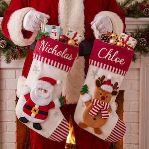 May include: Two white Christmas stockings with red striped cuffs and toes. One stocking features the name Nicholas and a plush Santa Claus applique. The other stocking features the name Chloe and a plush reindeer applique wearing a red and white scarf.