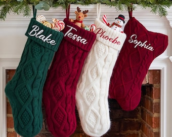 May include: Four cable-knit Christmas stockings in dark green, deep red, white, and burgundy. Each stocking features a white embroidered name: Blake, Tessa, Phoebe, and Sophia. The stockings are filled with small toys and candy canes.