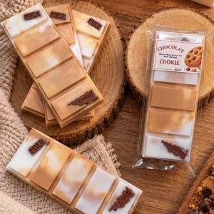 Peut inclure: Tablettes de cire rectangulaires au fini marbré blanc et beige, avec le texte en relief MILK et COOKIE. Une tablette est scellée dans un emballage plastique transparent avec une étiquette CHOCOLAT COOKIE et une image de biscuit.