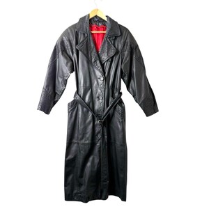 May include: A long black leather trench coat featuring a notched collar, long sleeves with textured panels, a button-front closure, and a matching tie belt at the waist. The interior of the coat is lined with a vibrant red fabric.