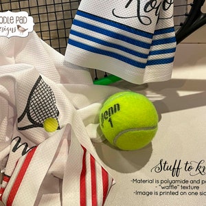 K&ouml;nnte beinhalten: Wei&szlig;es K&uuml;chentuch mit einem Tennisracket- und Ball-Design. Das Tuch hat eine Waffelstruktur und besteht aus Polyamid und Polyester. Das Bild ist nur auf einer Seite bedruckt.