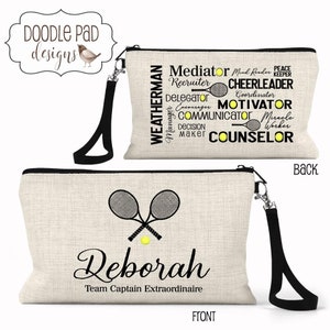 May include: A beige canvas zippered pouch with a black wrist strap. The front features a tennis racket and ball design with the name "Deborah" and "Team Captain Extraordinaire." The back displays words like "Mediator" and "Counselor."