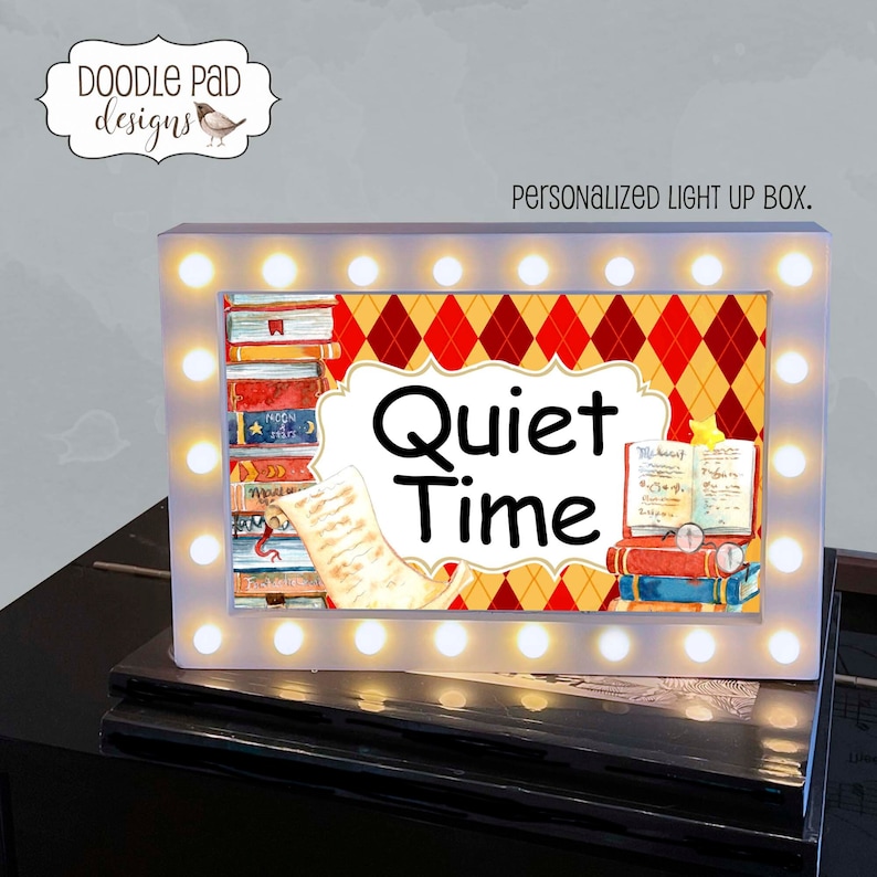 May include: A white light-up box with a red and yellow diamond pattern background. The box has a white border with a row of white lights around the edge. The box says "Quiet Time" in black text with a stack of books and a scroll on either side.