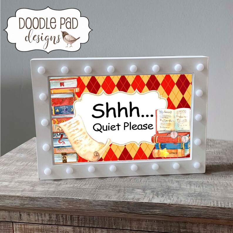May include: A white sign with a light-up border featuring a stack of books, a scroll, and a red and yellow diamond pattern. The sign reads "Shhh... Quiet Please".