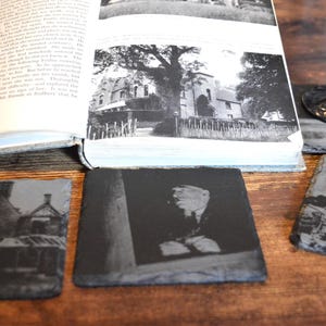 May include: Four black slate coasters with different images printed on them. The images include a house, a building, a person, and a building with a tree in front of it.