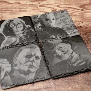 May include: Four square slate coasters featuring laser-engraved horror movie characters. One shows Chucky, one shows Jason Voorhees with a sign reading Welcome to Camp Crystal Lake Est 1935, one shows Michael Myers, and one shows Freddy Krueger.