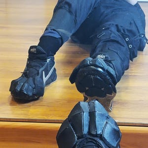 Puede incluir: Pantalones cargo negros y zapatillas deportivas negras con logotipos swoosh plateados. Las zapatillas cuentan con accesorios personalizados de espuma negra sobre las zonas de los dedos y el antepi&eacute;, creando un aspecto segmentado y blindado.