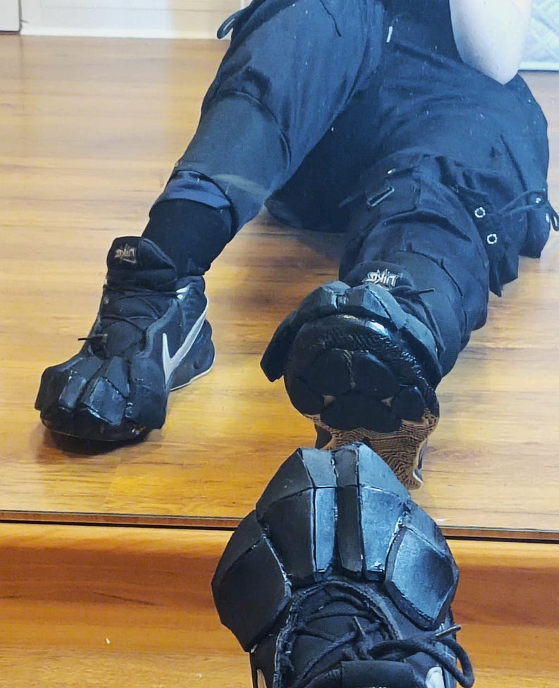 Puede incluir: Pantalones cargo negros y zapatillas deportivas negras con logotipos swoosh plateados. Las zapatillas cuentan con accesorios personalizados de espuma negra sobre las zonas de los dedos y el antepi&eacute;, creando un aspecto segmentado y blindado.