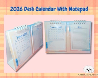 May include: A desk calendar for 2026 with a notepad section. The calendar is white with a blue and pink watercolor design. The calendar shows the month of January. The notepad section has lined pages.
