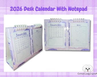 Puede incluir: Calendario de escritorio 2026 con bloc de notas. El calendario es de color lila claro con encuadernación en espiral blanca. Muestra el mes de enero y una sección de notas. El fondo tiene un patrón lila claro.