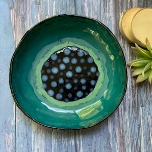 May include: A teal ceramic bowl with a black and white polka dot design in the center. The bowl has a glossy finish.