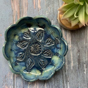 May include: A blue and green ceramic dish with a scalloped edge and a raised floral design. The dish is decorated with gold dots.