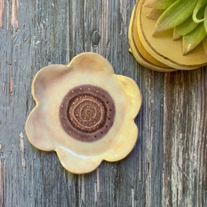 May include: A ceramic flower-shaped dish with a swirl design in shades of purple and gold. The dish is white with a slightly textured surface.