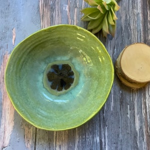 May include: A large, green ceramic bowl with a dark green and black center. The bowl has a glossy finish and is perfect for serving salads, pasta, or other dishes.