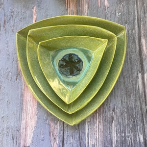 May include: Three green triangular ceramic plates nested together. The smallest plate has a blue and green glaze with a dark gray design in the center.