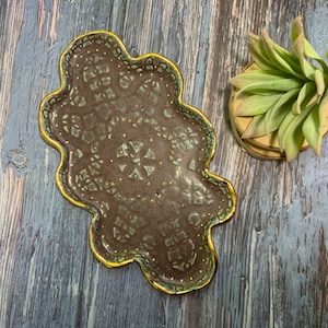 May include: A brown ceramic tray with a green and gold design. The tray has a wavy edge and is perfect for serving snacks or jewelry.