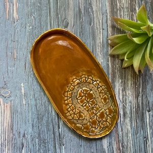 May include: A brown oval ceramic dish with a gold rim and a decorative design of a snake and a floral pattern.