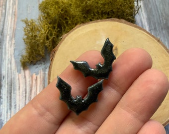 May include: A pair of black bat-shaped earrings with glitter embedded in the resin.
