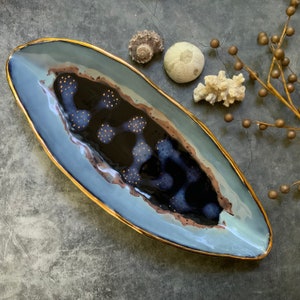 May include: A long, oval serving dish with a blue and black glaze. The dish has a gold rim and a speckled design.