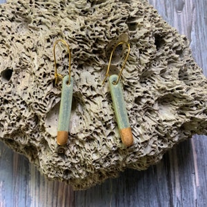 May include: A pair of green and gold ceramic earrings with gold hooks. The earrings are rectangular in shape and have a textured surface.